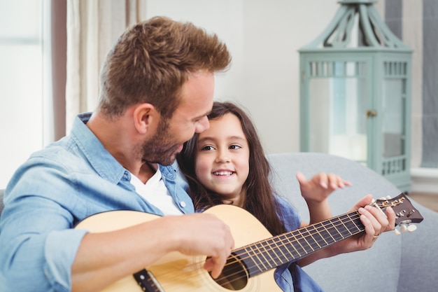 Homem tocando violão com sua filha em casa