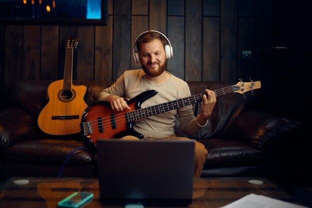 Homem tocando violão, ouvindo, olhando para o laptop