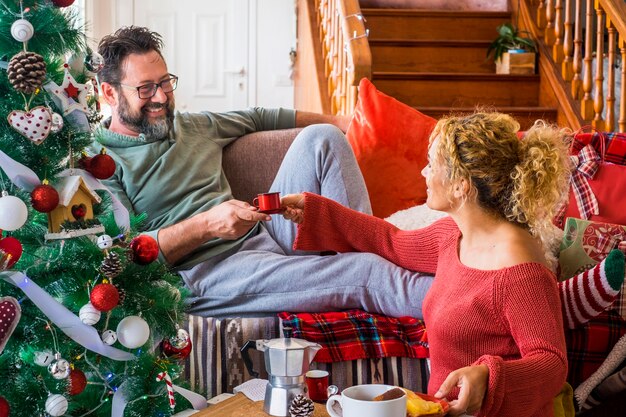 Homem tomando a xícara de café de sua esposa durante a celebração de natal em casa. casal caucasiano tomando café da manhã na véspera da celebração do natal. casal na sala de estar com árvore de natal decorada.