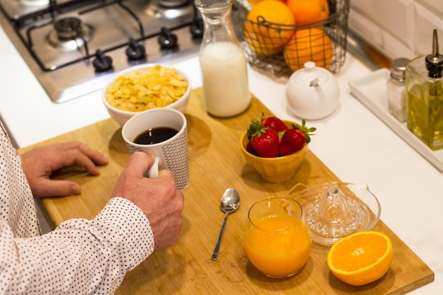 Homem tomando café da manhã com uma xícara de café e suco de laranja