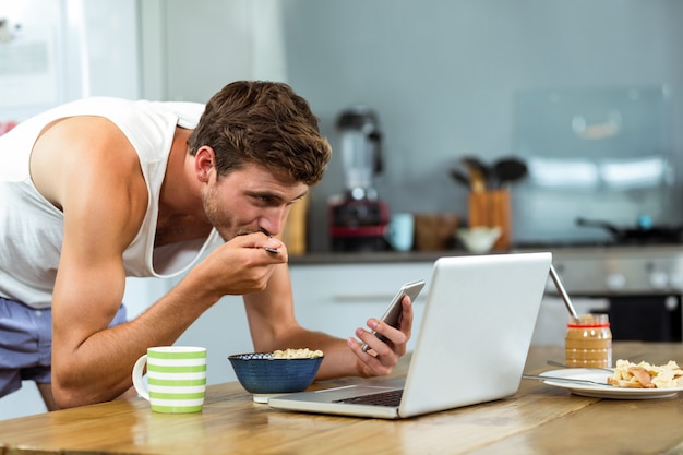 Homem tomando café da manhã enquanto estiver usando o celular na cozinha