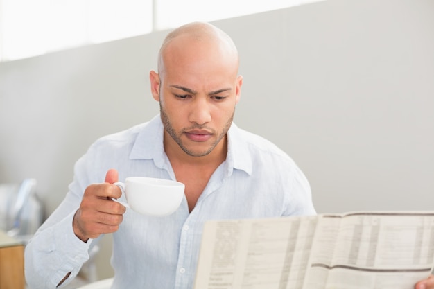 Homem tomando café enquanto lê jornal em casa