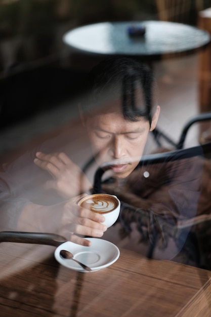Homem tomando café visto através de uma janela de vidro