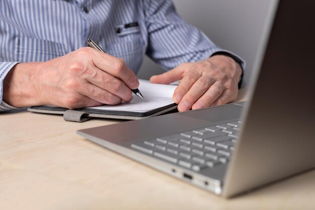 Homem tomando notas no planejador e usando laptop para educação on-line mãos de trabalho distantes closeup man wri