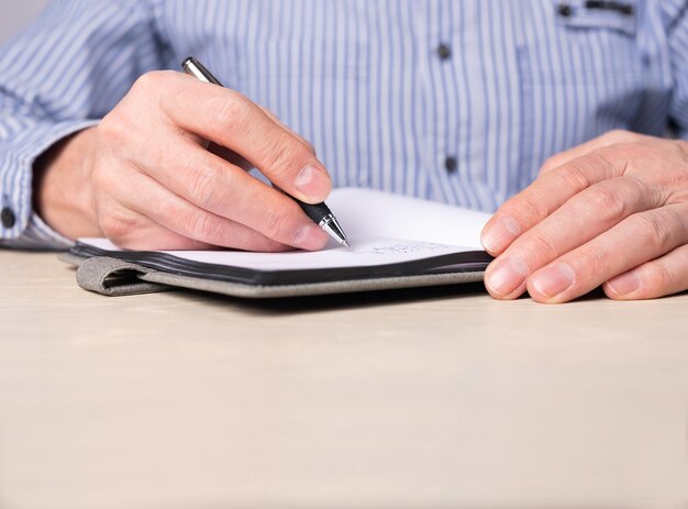 Homem tomando notas no planejador Mãos fechadas escrevendo lembretes de agenda de informações com caneta no caderno Empresário sentado na mesa e trabalhando ou estudando
