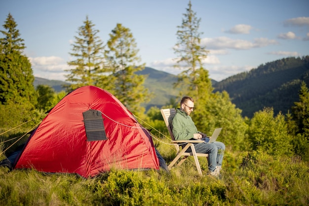 Homem trabalha no laptop no acampamento nas montanhas