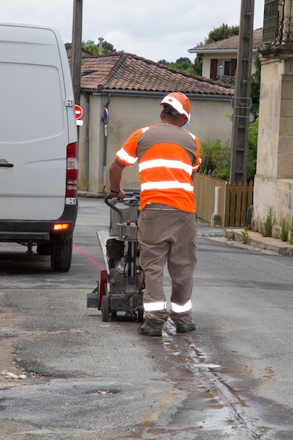 Homem trabalhador em um canteiro de obras de estrada corta o alcatrão com uma máquina