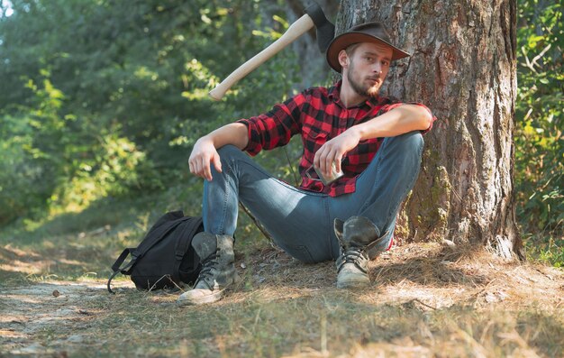 Homem trabalhador lenhador sentado na floresta lenhador com machado no fundo da floresta homem fazendo homem