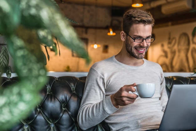 Homem trabalhando em seu laptop e bebendo café da manhã no café