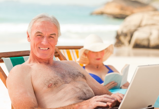 Homem trabalhando em seu laptop enquanto sua esposa lê na praia