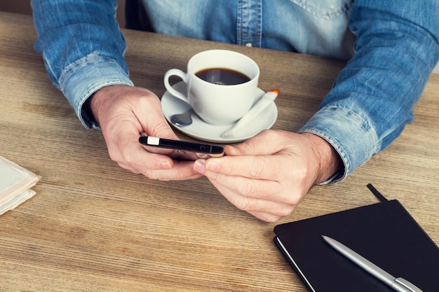 Homem trabalhando em sua mesa com um smartphone e uma xícara de café