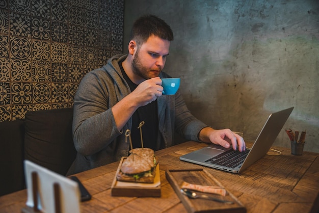 Homem trabalhando no laptop no café café da manhã sanduíche e café