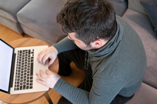 Homem trabalhando online em casa usando laptop no sofá