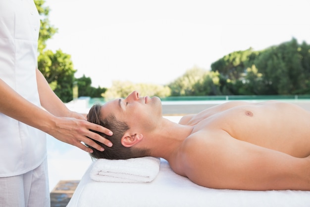 Homem tranquilo recebendo uma massagem na cabeça ao lado da piscina