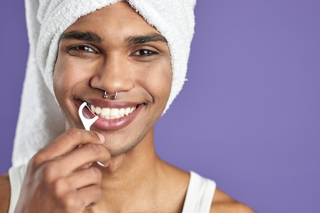 Homem transgênero com fio dental sorrindo em retrato isolado de fundo roxo.