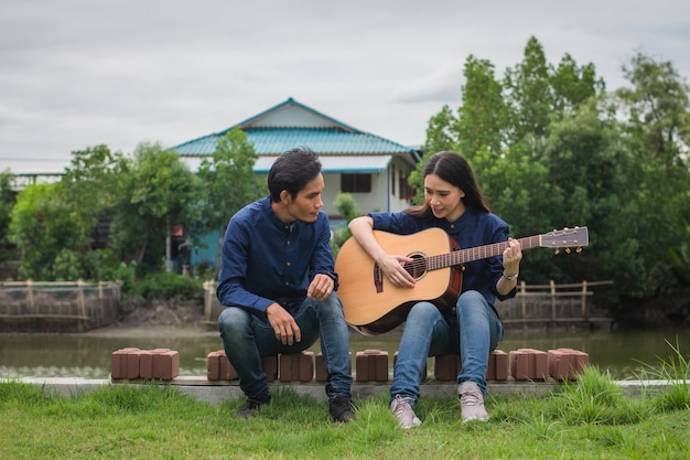 Homem treinando guitarra com a mulher sentada no parque natureza, descanso, férias de verão