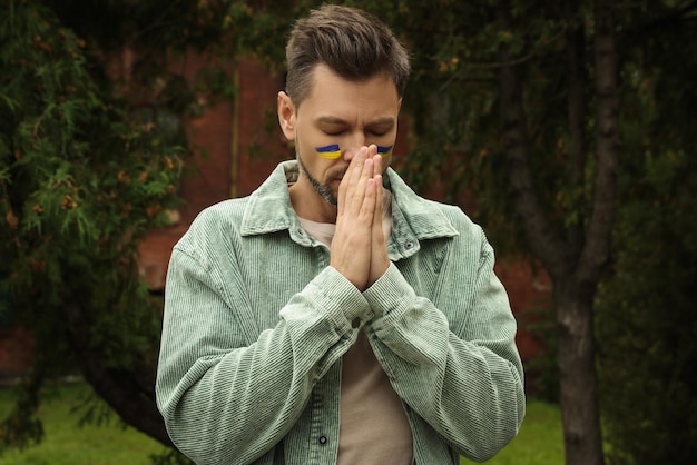 Homem triste com desenhos da bandeira ucraniana no rosto ao ar livre