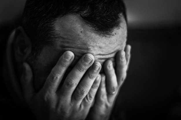 Homem triste de close-up cobrindo o rosto com as mãos