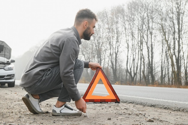 Homem triste na estrada ao lado do carro quebrado