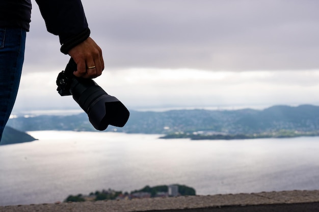 Homem turista irreconhecível com câmera na mão e ao fundo a cidade de Bergen e o fiorde na Noruega