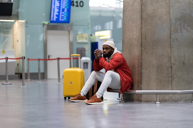 Homem turista negro cansado em uma longa conexão noturna no aeroporto esperando avião sentado no terminal