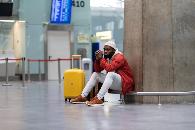 Homem turista negro cansado em uma longa conexão noturna no aeroporto esperando avião sentado no terminal