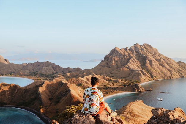 Homem turista sentado na rocha enquanto aprecia a vista das colinas e do mar na Ilha Padar