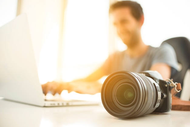 Homem turva usando laptop atrás da câmera dslr na mesa