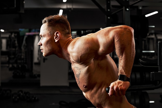 Homem, um atleta está envolvido em uma academia, fazendo um exercício sobre os músculos dos braços, bíceps, fundo preto. Foto de alta qualidade.