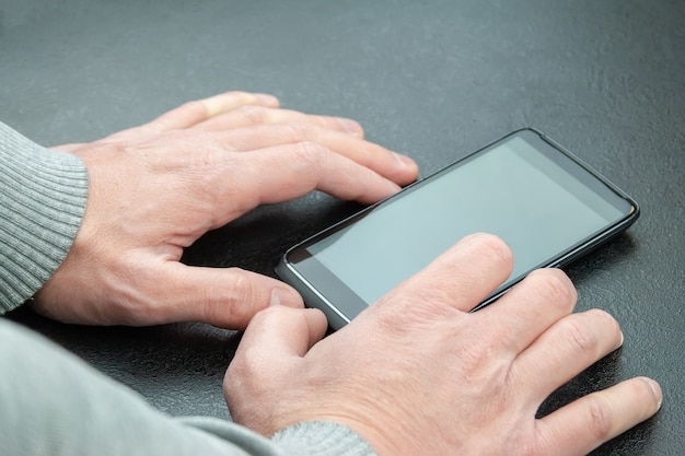 Homem usa um celular que está sobre a mesa