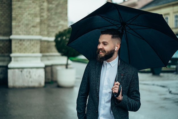 Homem usando airpods enquanto segura um guarda-chuva preto