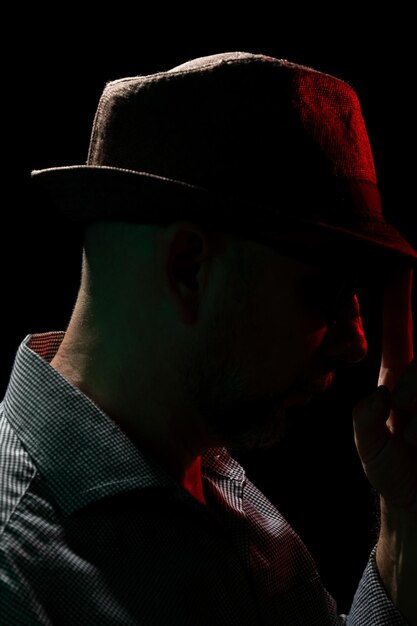 Homem usando chapéu e óculos de sol na escuridão com luz vermelha no rosto