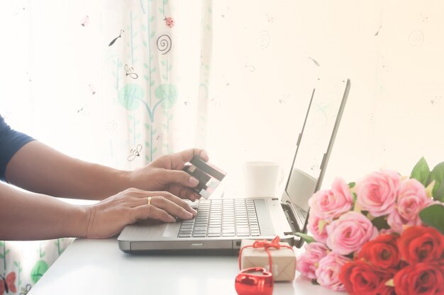 Homem, usando computador, e, cartão crédito, com, presente, e, rosas, ligado, tabela