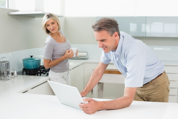 Homem usando laptop com mulher na cozinha