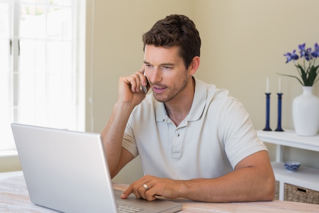 Homem usando laptop e celular em casa