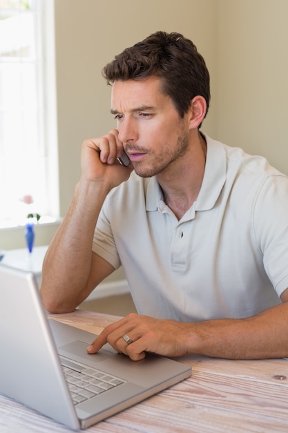 Homem usando laptop e celular em casa