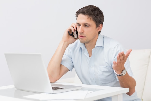 Homem usando laptop e celular na sala de estar