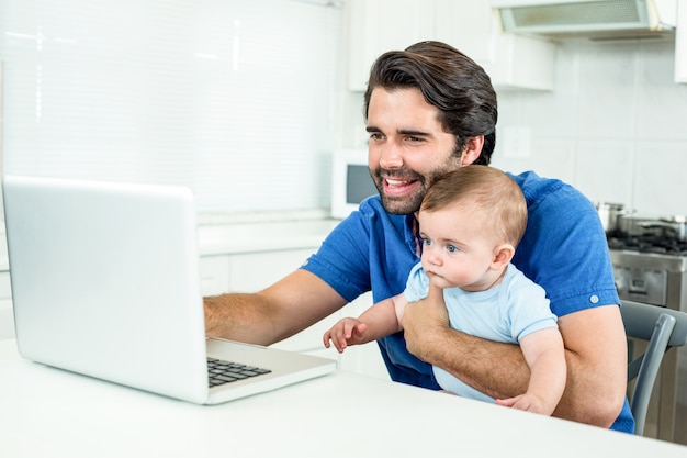 Homem usando laptop enquanto está sentado com o filho na mesa