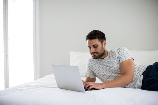 Homem usando laptop na cama no quarto