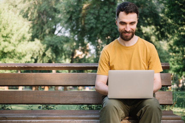 Homem usando laptop, sentado no banco. freelancer trabalhando no parque, digitando no teclado