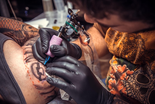 Homem usando luvas mostrando o processo de fazer uma tatuagem no salãotattooer fazendo uma tatuagem no estúdio de tatuagem