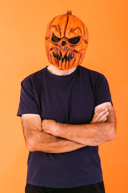 Foto homem usando máscara de látex de abóbora assustadora com t-shirt azul com os braços cruzados, em fundo laranja. halloween e dias do conceito morto.