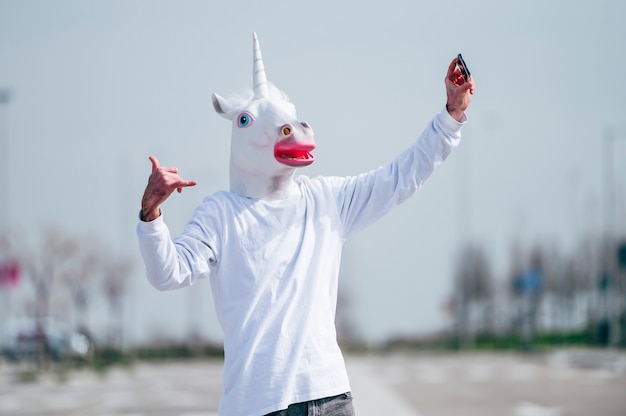 Foto homem usando máscara de unicórnio tirando foto com smartphone