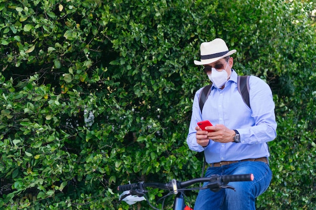 Homem usando máscara protetora verificando o celular enquanto anda de bicicleta
