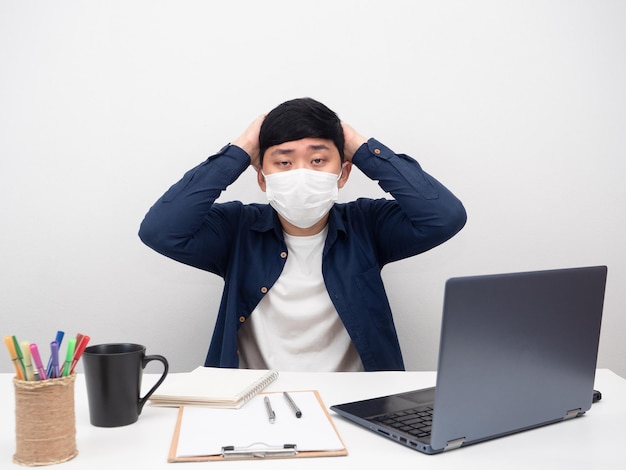 Homem usando máscara sentado no local de trabalho sente dor de cabeça sobre o trabalho