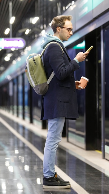 Homem usando o celular, esperando o trem na estação de metrô
