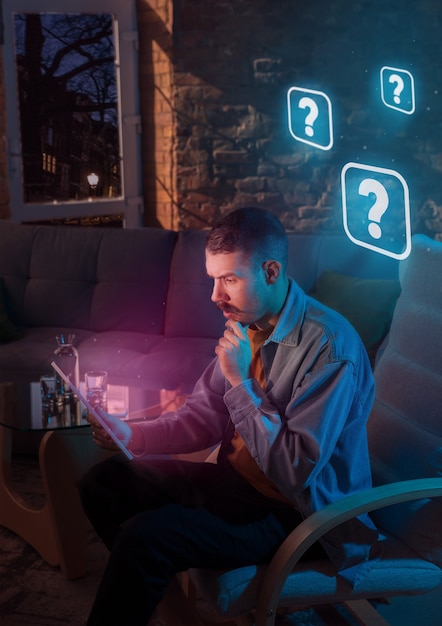 Homem usando o gadget e receber notificações de néon em casa à noite. Sentado na poltrona, servindo na internet e procurando informações. Abuso de mídia social, bate-papo e navegação, vício em gadgets.