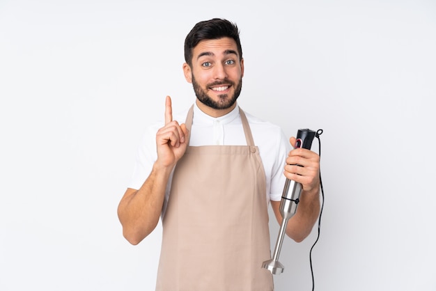 Homem usando o liquidificador na parede branca, apontando com o dedo indicador