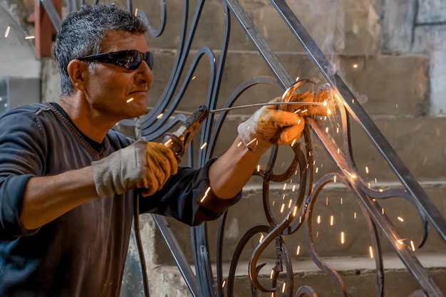 Foto homem usando óculos de proteção solda metal com máquina de solda em uma casa particular, closeup