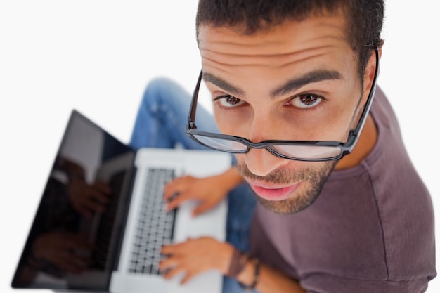 Homem usando óculos sentado no chão usando o laptop e olhando para a câmera